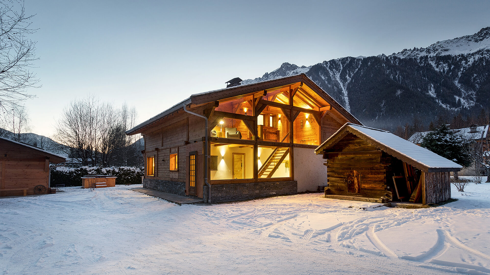 Hyggeligt chalet med aftenbelysning i snefyldt landskab med udsigt til flotte bjerge